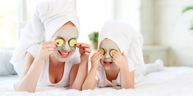 Mother and child with natural face masks on, covering eyes with cucumber slices.