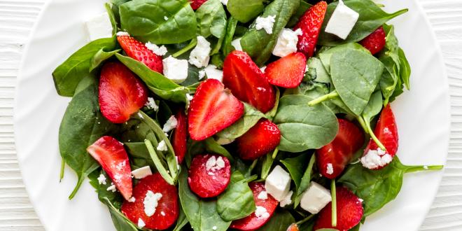 a plate of spinach, crumbled feta, and sliced strawberries