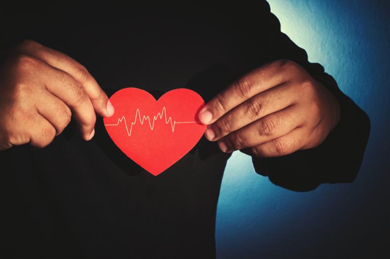A person in a black sweater holds a red heart cut-out over their chest.
